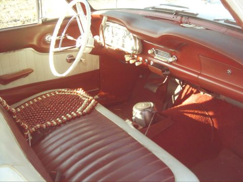 1962 Ford Falcon - The interior of a 1962 Ford Falcon features red upholstery, a white steering wheel, and a classic dashboard layout.