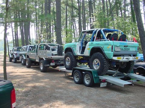 1969 Ford Bronco - Several off-road vehicles are lined up, with a teal Ford Bronco being transported on a trailer.