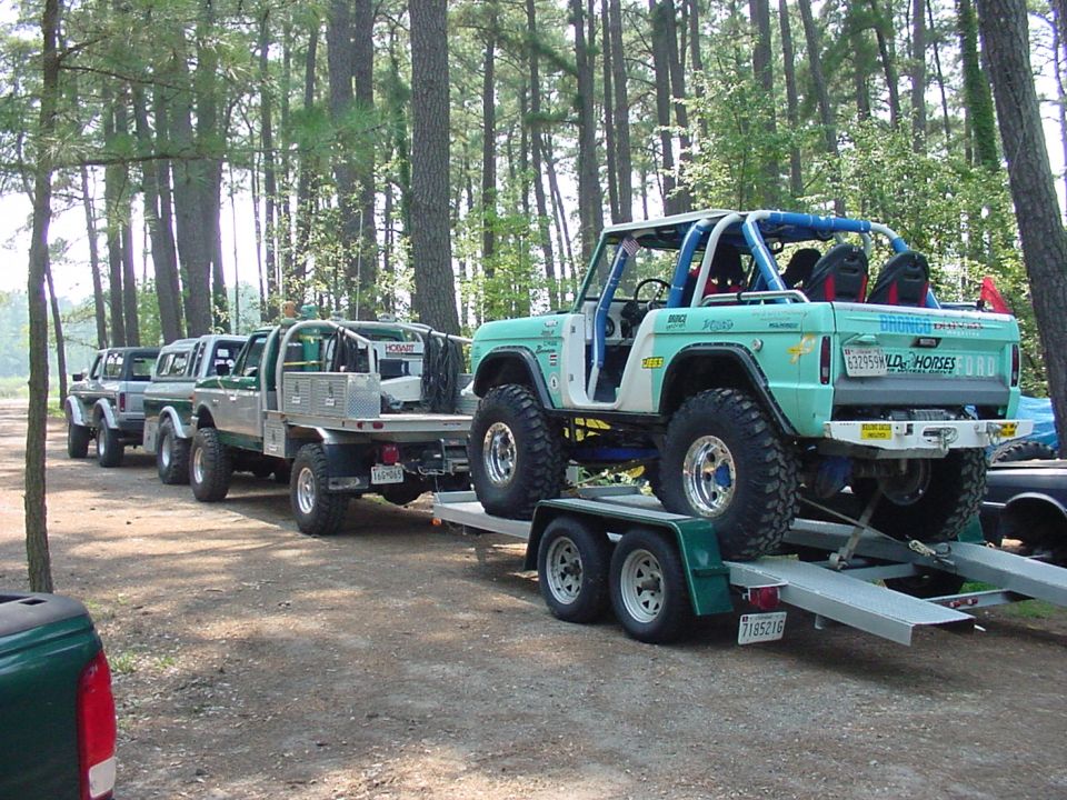 Teal Ford Bronco with roll cage on a trailer, other trucks in background