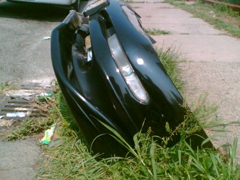 1997 Ford Probe - A damaged black car bumper with a headlight is discarded by the roadside.