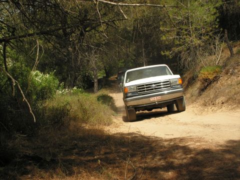 1988 Ford Bronco - White Ford F-Series truck navigates a dusty path with another vehicle following.