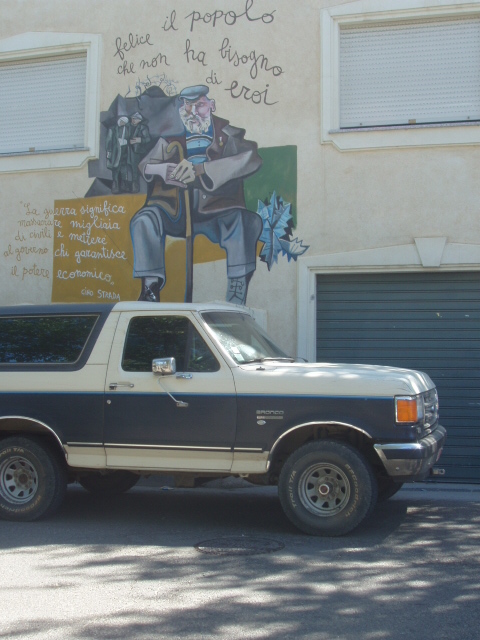 1988 Ford Bronco - A two-tone Ford Bronco is parked on a street in front of a building a mural of an old man.