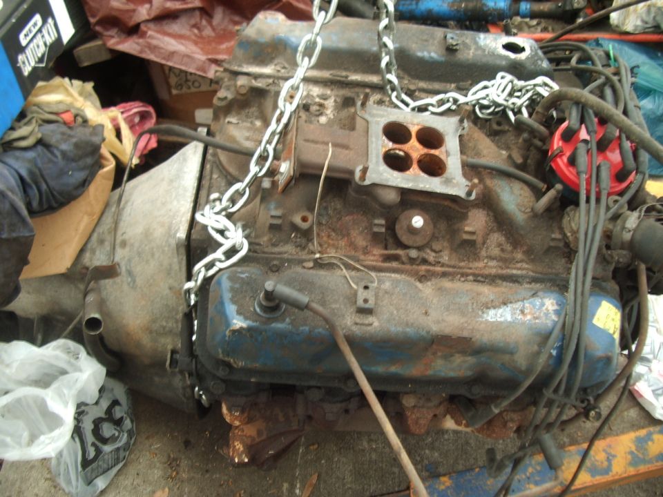 V8 engine block with carburetor, distributor, and spark plug wires. Chain attached for lifting