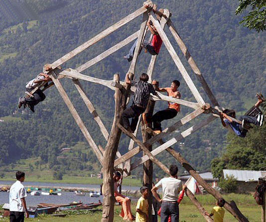 Wooden swing structure with people riding, overlooking a lake and mountains