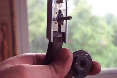 1985 Ford LTD Crown Victoria - A hand holds a car part, possibly a window regulator mechanism, against a blurred outdoor background.