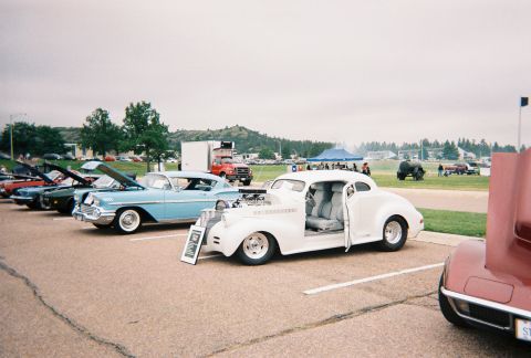 1972 Ford Ranchero - Several cars are parked in a lot under an overcast sky, with tents and trees in the background.