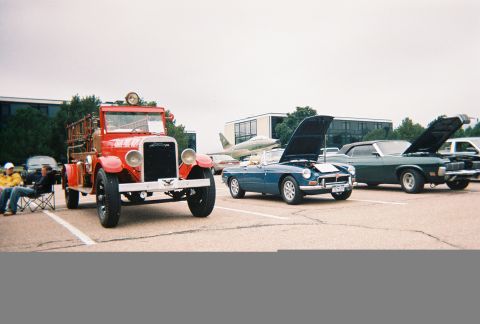 1972 Ford Ranchero - A vintage red fire truck is parked at an outdoor car show with other vehicles and an airplane in the background.