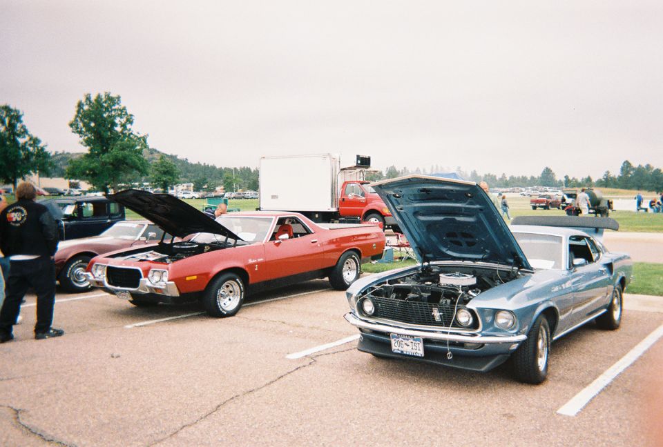 Red Ford Ranchero and silver-blue Mustang fastback with hoods up at outdoor car show