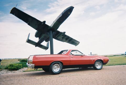 1972 Ford Ranchero - A red 1972 Ford Ranchero is parked on a road with a large airplane monument in the background.