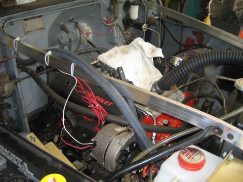 1990 Ford Bronco - in-progress engine bay shows a red Chevrolet engine with alternator, hoses, and wiring beneath a metal brace.