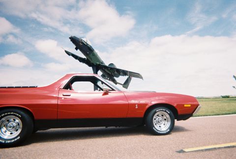 1972 Ford Ranchero - A red 1972 Ford Ranchero is parked on asphalt with an airplane display in the background under a cloudy sky.