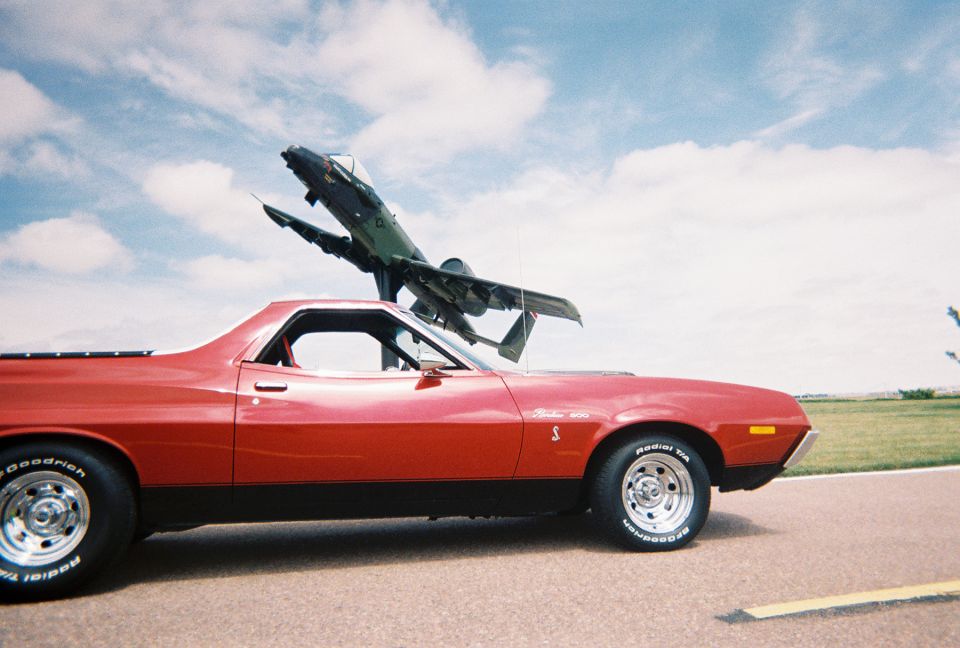 Red Ford Ranchero 500 side profile beneath a pole-mounted static display jet