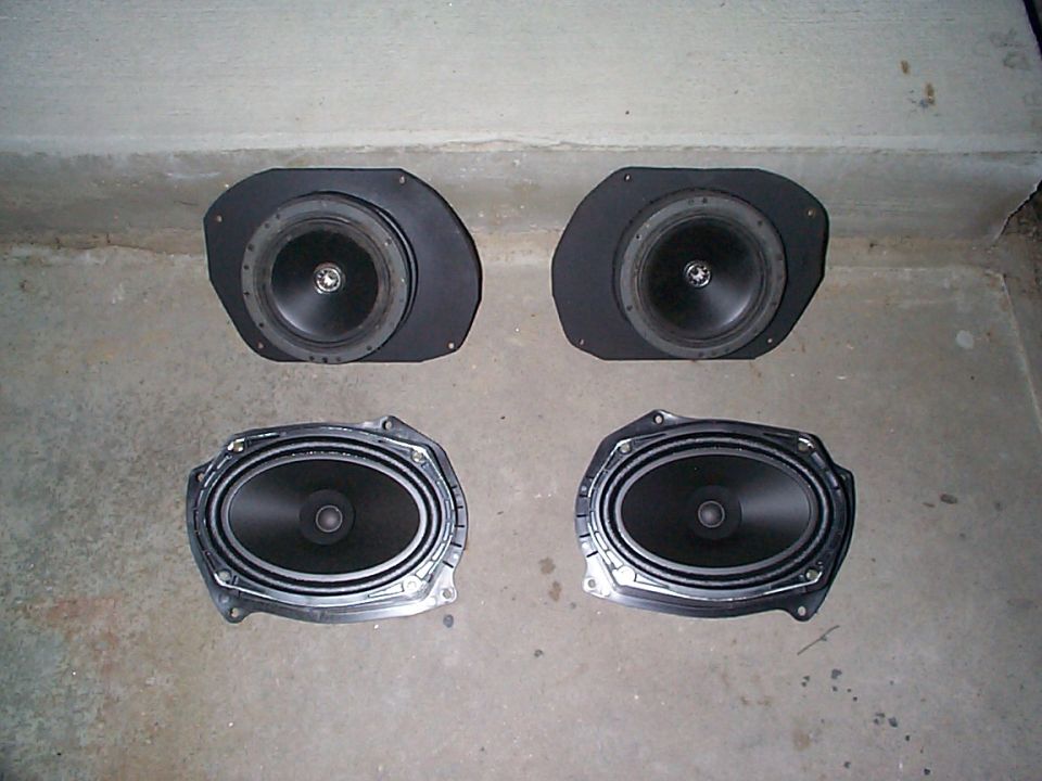 Four car speakers laid out on a concrete floor. Two are round, and two are oval