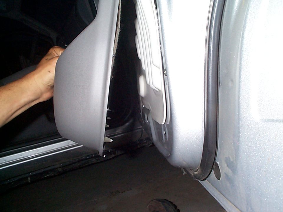 Gray interior door panel removed from a silver vehicle, revealing internal components. A hand is visible holding the panel
