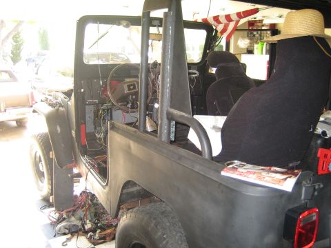 1990 Ford Bronco - topless off-road vehicle sits in a garage mid-restoration, showing bare metal tub, bucket seats and a tangle of exposed wiring.