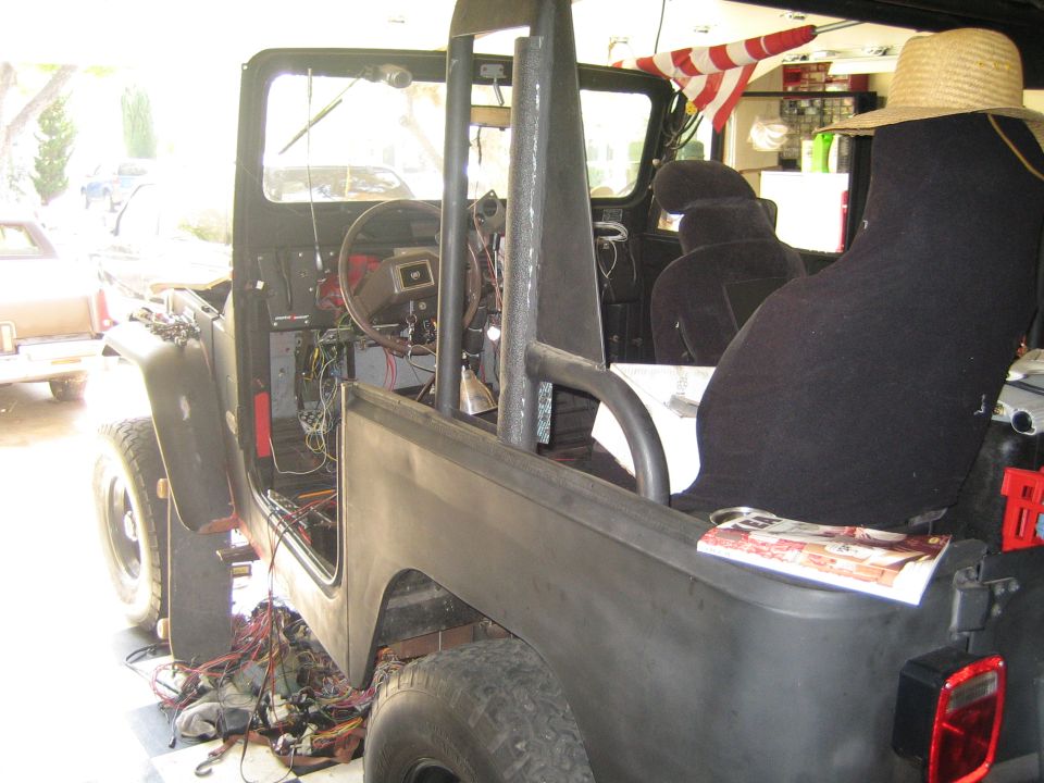 Open-top off-road vehicle mid-build in a garage, interior gutted with exposed wiring and bucket seats