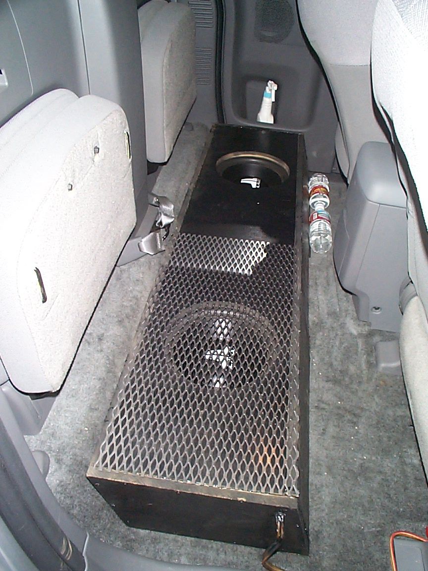 Aftermarket subwoofer box installed behind rear seats of a vehicle. Water bottles are on the floor
