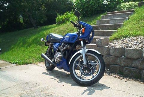 1985 Ford LTD Crown Victoria - A blue Suzuki motorcycle is parked on a driveway next to a stone wall and outdoor stairs.