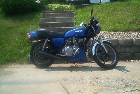 1985 Ford LTD Crown Victoria - A blue Suzuki motorcycle is parked outdoors next to a set of stairs and a stone wall.