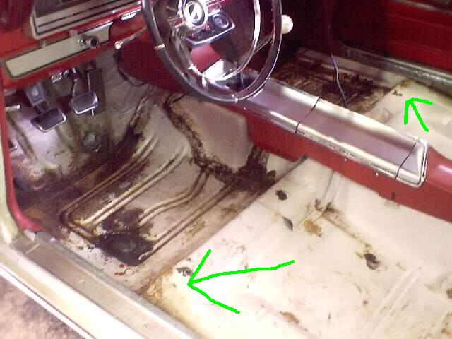 Stripped interior floor pan with dirt and rust spots, green arrows marking problem areas, red dash visible