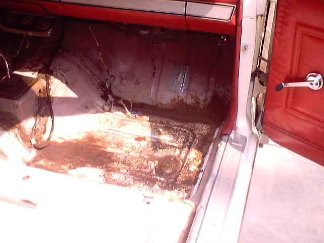 Stripped interior of 1966 Ford Fairlane showing rusty bare floor pan, red dash and door panel