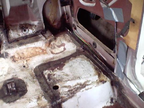 1966 Ford Fairlane - Car interior floor pan with rust and dirt, showing wiring and a maroon panel section.