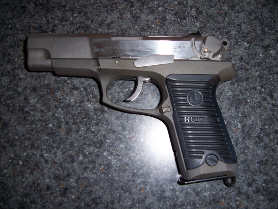 Stainless and black Ruger semi-automatic pistol lying on gray carpet, left side facing up