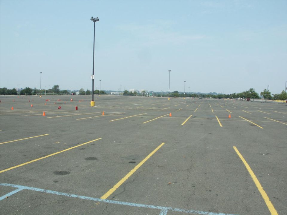 Empty asphalt parking lot with yellow lines and orange autocross cones under a hazy sky