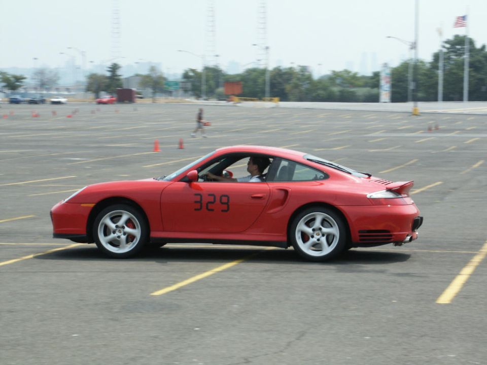 Red Porsche 911 Turbo with number 329 running an autocross course in a parking lot