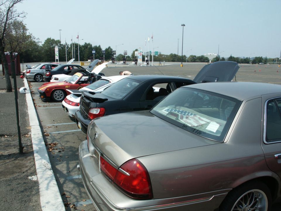 Row of cars parked along a curb with hoods open, gold Jaguar XJ sedan in foreground