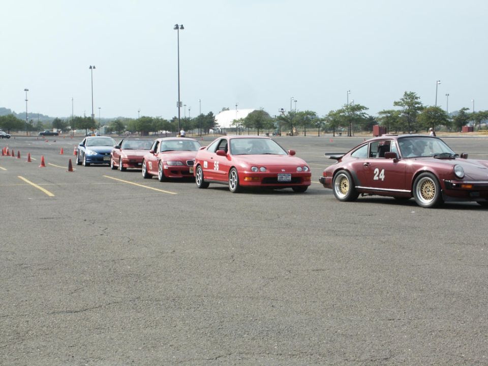 Grid of red cars lined up at autocross, including an Acura Integra and a Porsche 911 number 24