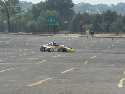 2001 Mercury Grand Marquis - A yellow open-wheel race car is seen in a large, empty parking lot with trees in the background.