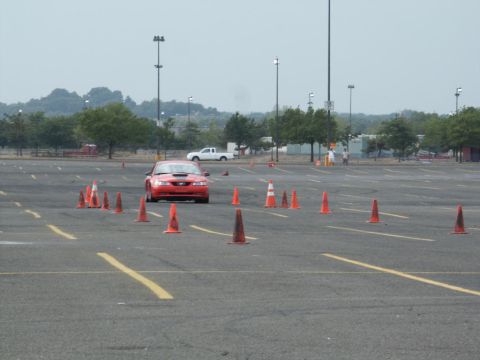 2001 Mercury Grand Marquis - A red sports car navigates an obstacle course marked by orange cones in a large parking lot.