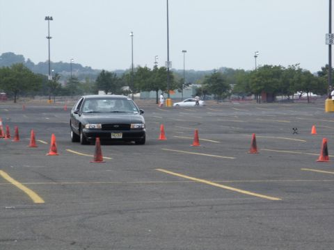 2001 Mercury Grand Marquis - A black sedan drives through an autocross course marked by orange cones in a large paved area.