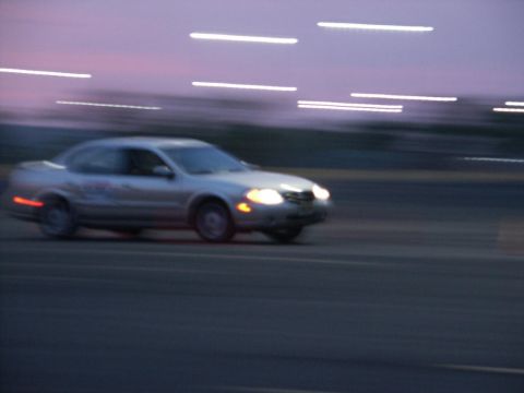 2001 Mercury Grand Marquis - A silver sedan drives on a road at dusk with motion blur and illuminated headlights.
