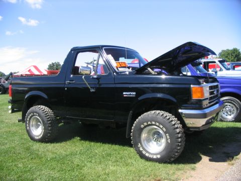 1986 Ford Bronco - This black Ford Bronco is displayed with its hood up at an outdoor event, with other vehicles visible.
