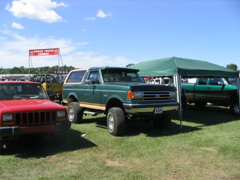 1986 Ford Bronco - A green Ford Bronco with tan trim is parked on a grassy field next to other vehicles and a green tent.