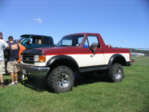 1986 Ford Bronco - This two-tone Ford Bronco is parked on a grassy field next to another vehicle.