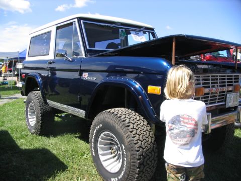 1986 Ford Bronco - A dark blue Ford Bronco is displayed at an outdoor event with its hood open.