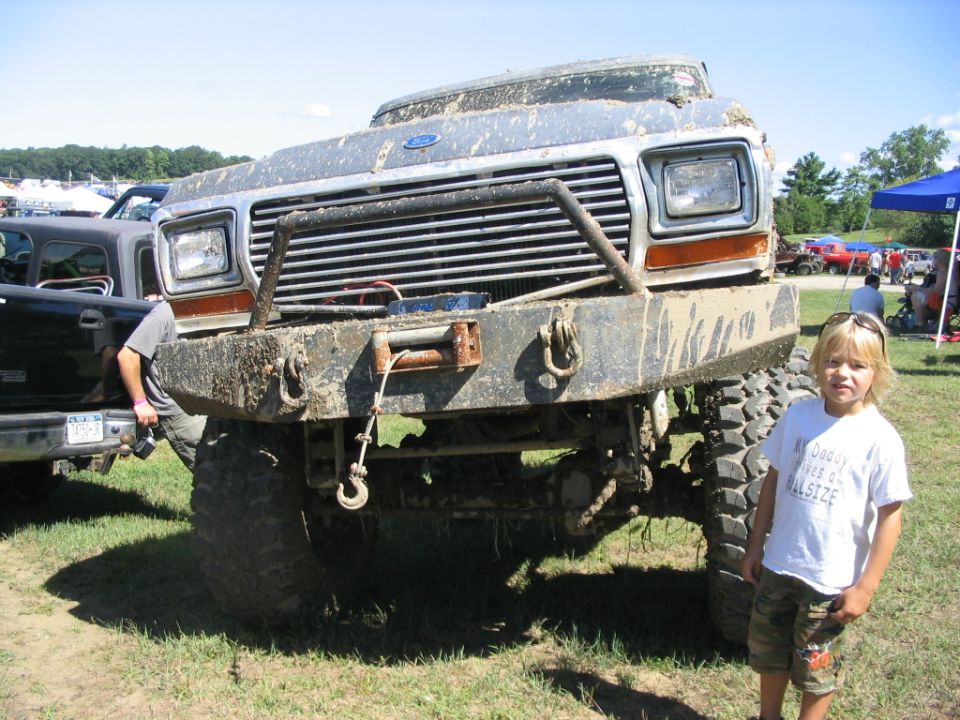 Mud-covered 1980s Ford truck front end with winch; child stands to the right