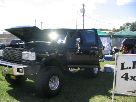 1986 Ford Bronco - This black Ford Bronco has its hood and driver door open, revealing its engine and interior at an outdoor event.