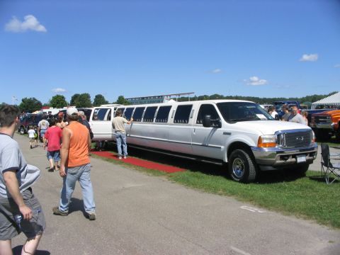 1986 Ford Bronco - A long white limousine is displayed at an outdoor event, with people walking nearby.