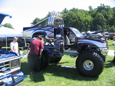 1986 Ford Bronco - A heavily modified pickup truck with extreme lift and large tires is on display at an outdoor event.