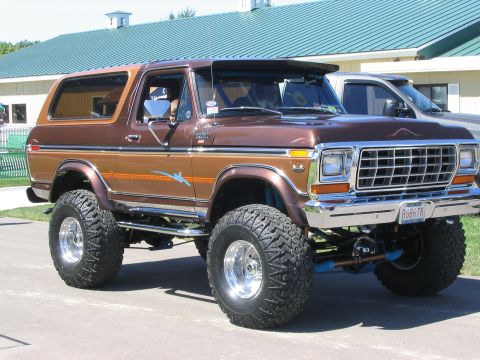 1986 Ford Bronco - This lifted 1986 Ford Bronco features a two-tone brown paint scheme and prominent chrome accents, parked at an outdoor event.