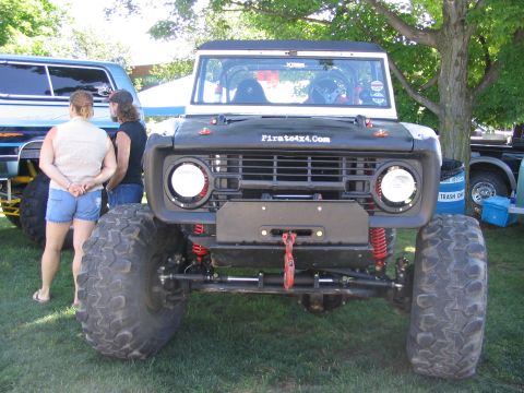 1986 Ford Bronco - A heavily modified Ford Bronco is displayed outdoors, with other vehicles and people nearby.