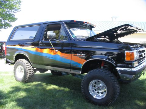 1986 Ford Bronco - This lifted Ford Bronco displays custom graphics and has its hood open at an outdoor event.