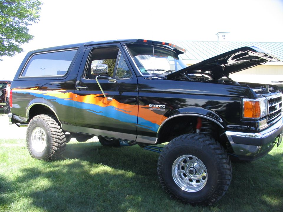Black Ford Bronco with orange and blue graphics, hood up, lifted suspension, chrome wheels