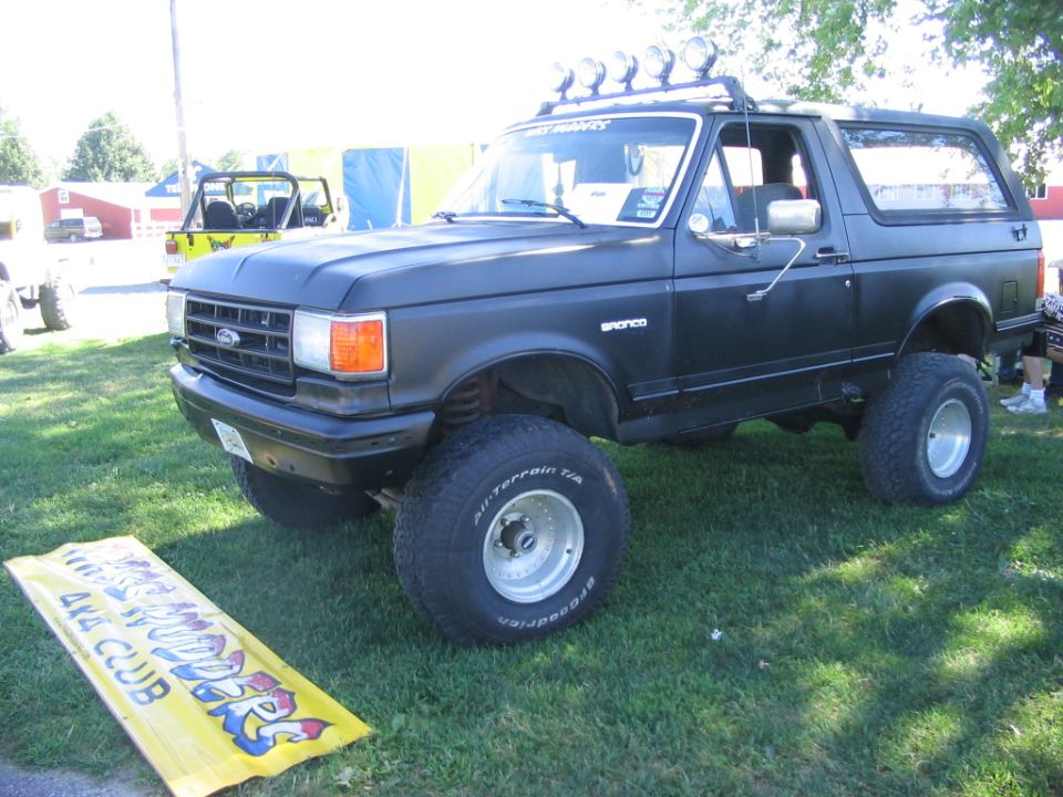 Flat-black lifted Ford Bronco on white wheels with roof light bar at a 4x4 club show