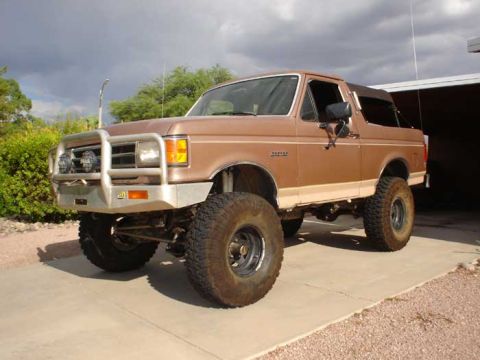 1989 Ford Bronco - Brown 1989 Ford Bronco modified for off-road use sits parked outside a garage.