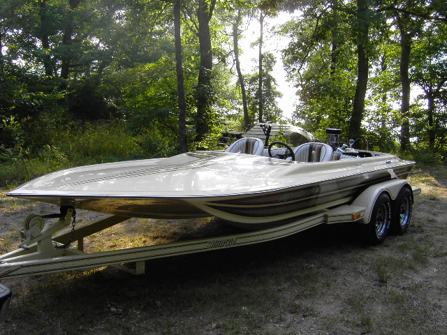 Cream and gold jet boat on a tandem-axle trailer parked in a wooded clearing